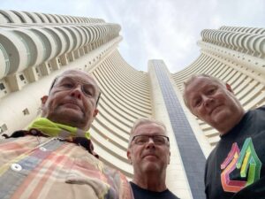 Three men outside infront of a building looking down